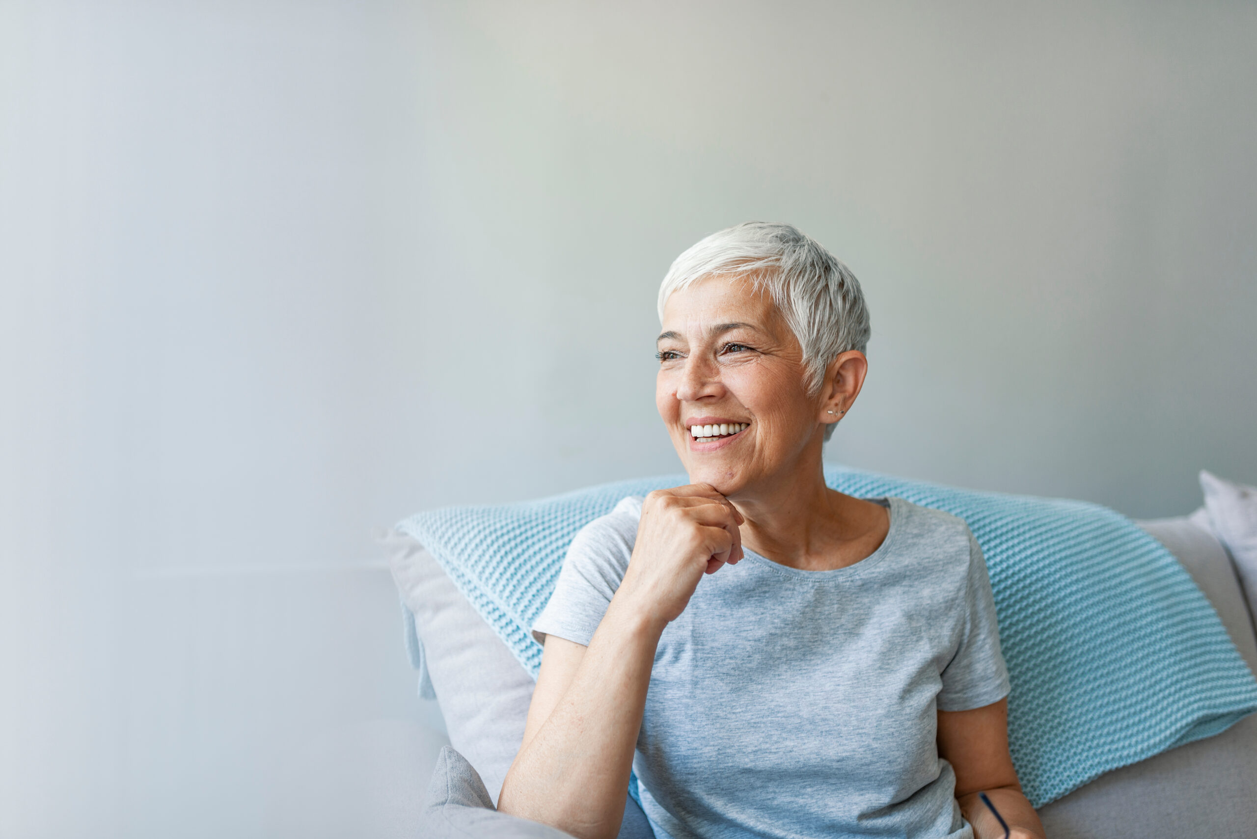 Eine ältere lachende Frau mit kurzen Haaren auf einem Sessel, mit dem Blick nach rechts